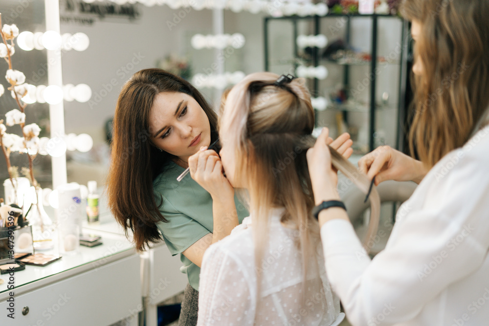 Two female make-up artist working with young woman model in dressing room. Concept of backstage work. Two female make-up artist working with young woman model in dressing room. Concept of backstage work.