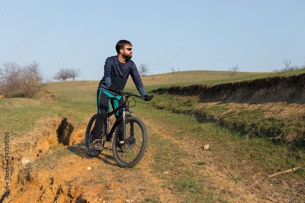 Cyclist in shorts and jersey on a modern carbon hardtail bike with an air suspension fork standing on a cliff against the background of fresh green spring forest