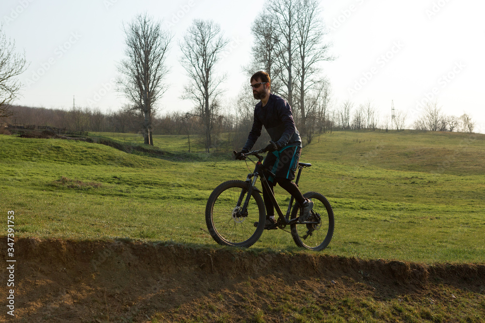 Cyclist in shorts and jersey on a modern carbon hardtail bike with an air suspension fork standing on a cliff against the background of fresh green spring forest Cyclist in shorts and jersey on a modern carbon hardtail bike with an air suspension fork standing on a cliff against the background of fresh green spring forest