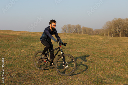 Cyclist in shorts and jersey on a modern carbon hardtail bike with an air suspension fork standing on a cliff against the background of fresh green spring forest