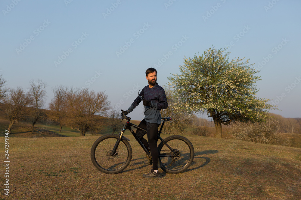 Cyclist in shorts and jersey on a modern carbon hardtail bike with an air suspension fork standing on a cliff against the background of fresh green spring forest Cyclist in shorts and jersey on a modern carbon hardtail bike with an air suspension fork standing on a cliff against the background of fresh green spring forest