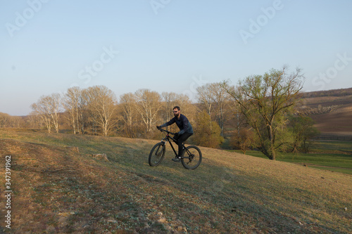 Cyclist in shorts and jersey on a modern carbon hardtail bike with an air suspension fork standing on a cliff against the background of fresh green spring forest