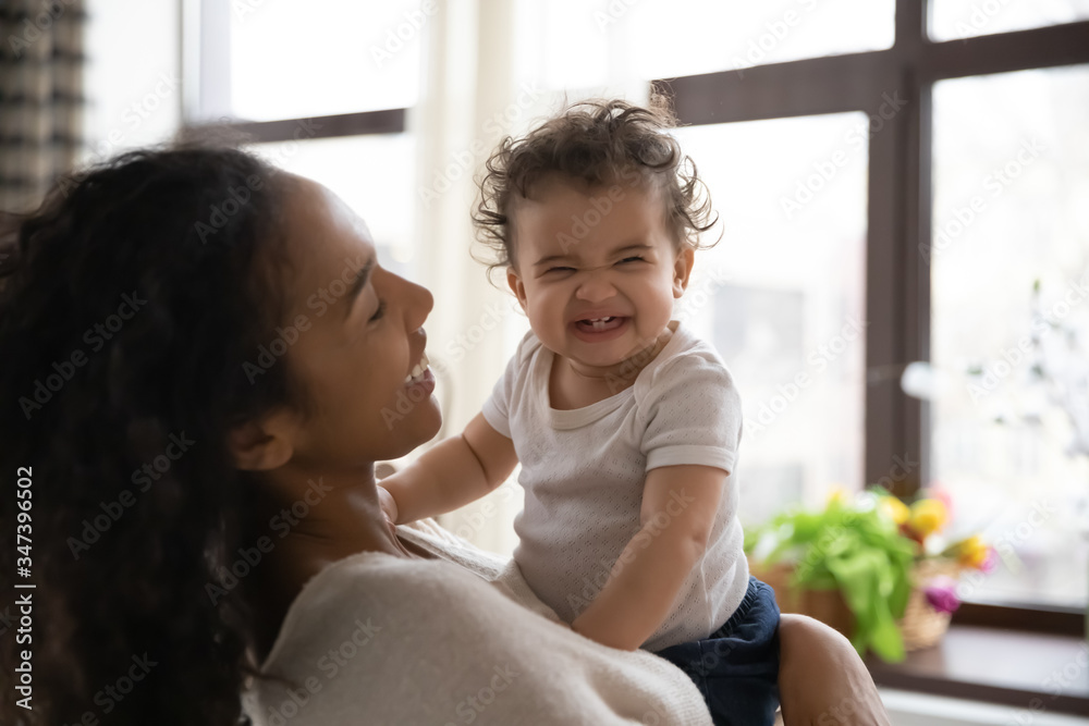Loving young african American mother hold in arms cute funny infant toddler showing first teeth, caring happy biracial mom hug embrace smiling little baby girl child, motherhood, childcare concept Loving young african American mother hold in arms cute funny infant toddler showing first teeth, caring happy biracial mom hug embrace smiling little baby girl child, motherhood, childcare concept