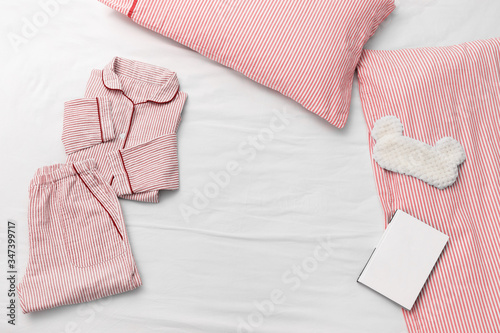 Sleepwear for slumber. Pink women pajama from cotton cloth with stripes, pillow, fluffy sleeping eye mask and book for reading before going to bed. Top view. Flat lay.