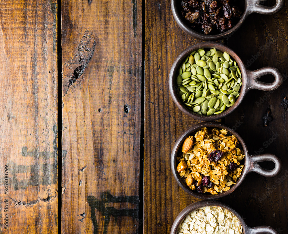 Variety of nuts, seeds and granola in a clay pots with a beautiful wooden rustic background. Healthy concept. Vegan Concept. Copy space. Top view