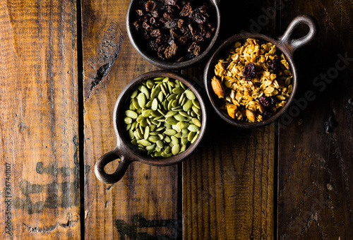 Variety of nuts, seeds and granola in a clay pots with a beautiful wooden rustic background. Healthy concept. Vegan Concept. Copy space. Top view