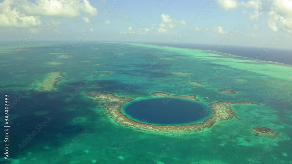 Aerial view of yacht next to large marine sinkhole against sky, scenic view of seascape on sunny day while drone moving backward - Great Blue Hole, Belize