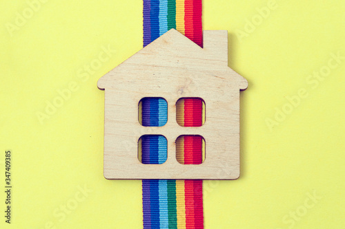 mini toy wooden house and lgbt rainbow ribbbon on yellow background photo