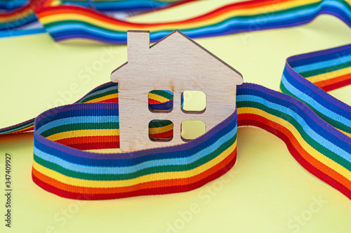 mini toy wooden house and lgbt rainbow ribbbon on yellow background photo