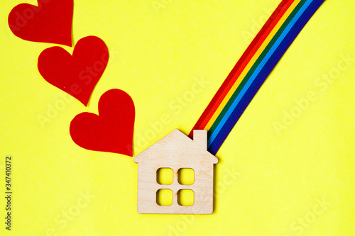 mini toy wooden house and lgbt rainbow ribbbon on yellow background photo