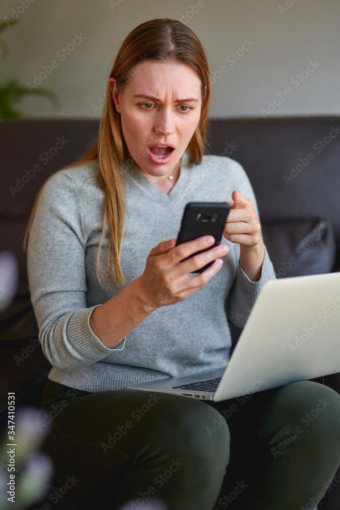 Sad woman sitting on sofa with laptop and talking on phone at home. College student studying on laptop and using phone. Sad woman sitting on sofa with laptop and talking on phone at home. College student studying on laptop and using phone.