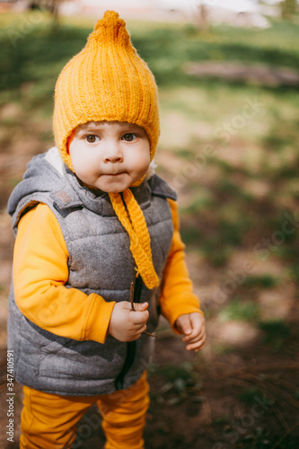 Stylish little one-year-old boy in a yellow hat, yellow pants and a gray jelly