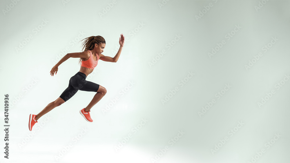 Never give up. Full length of young african woman with perfect body in sports clothing jumping in studio against grey background