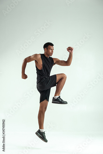 Do it Full length of young african man with muscular body in sports clothing jumping in studio against grey background