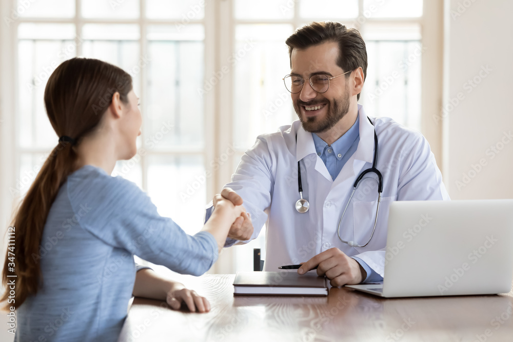 Obraz premium Smiling young Caucasian male doctor shake hand greeting get acquainted with female patient in hospital, happy man physician handshake woman client make agreement sign health insurance in clinic