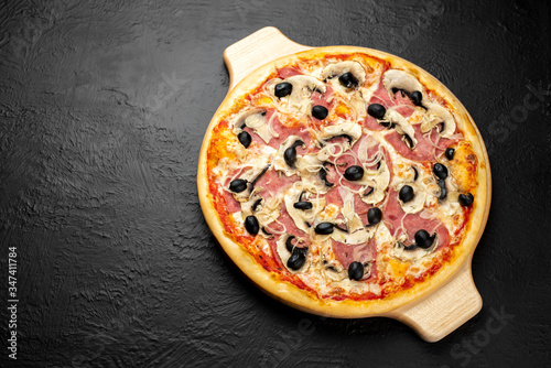 Milanese pizza on a black background, tomato-based with mozzarella, ham, mushrooms, onions and olives