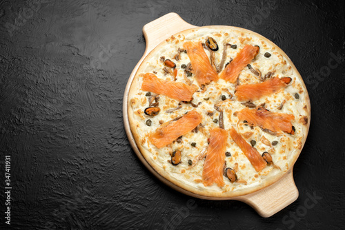Pizza NAPLES on a black background, cream-based with mozzarella, mussels, lightly salted salmon and capers