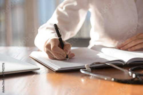 Close up of female doctor sit at desk in hospital filling patient form document, woman nurse or GP write in journal make notes of medical history or anamnesis of clinic client, healthcare concept