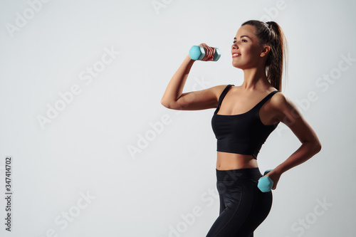 Fototapeta Naklejka Na Ścianę i Meble -  Girl Exercising with  Dumbbells Standing Front To Camera Over Gray Background