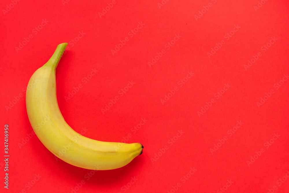 One yellow ripe banana on a plain red background. Tropical fruit. Healthy vegetarian food. Flat lay. Copy space One yellow ripe banana on a plain red background. Tropical fruit. Healthy vegetarian food. Flat lay. Copy space