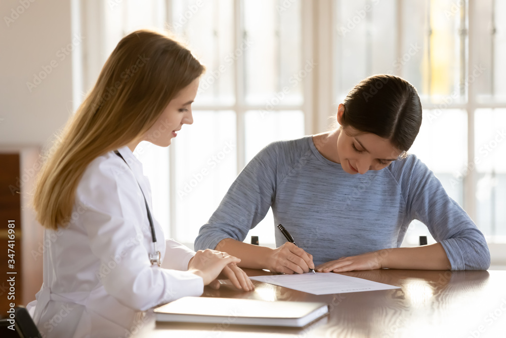 Young female patient sign paper document closing deal with GP in hospital, satisfied woman client put signature on paperwork make health insurance agreement with doctor in clinic, healthcare concept Young female patient sign paper document closing deal with GP in hospital, satisfied woman client put signature on paperwork make health insurance agreement with doctor in clinic, healthcare concept