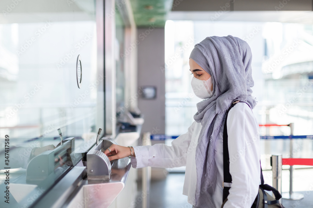 Asian muslim woman wearing medical mask for prevent dust and infection virus walking in buy passenger ticket at electric train station. Coronavirus(covid-19) concept. Asian muslim woman wearing medical mask for prevent dust and infection virus walking in buy passenger ticket at electric train station. Coronavirus(covid-19) concept.