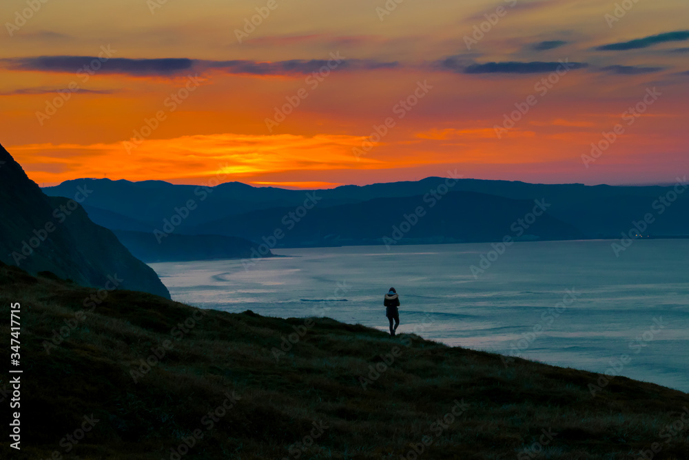 silhouette of a woman on the top of mountain looking to the sunset