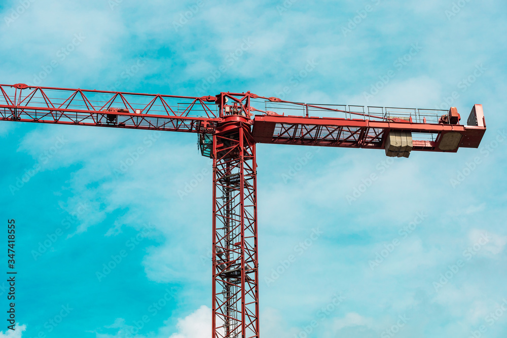 Red tower crane in horizontal position arrows against turquoise sky with white clouds. Close up. Copy space. backdrop Red tower crane in horizontal position arrows against turquoise sky with white clouds. Close up. Copy space. backdrop