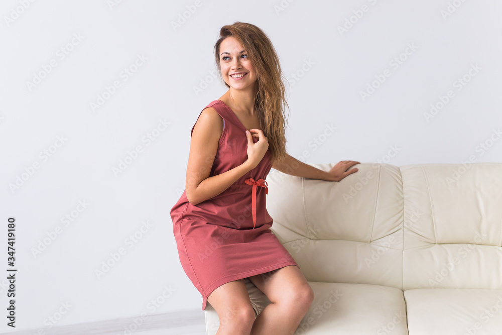 Young attractive woman dressed in beautiful home dress sitting on couch in her living room. Comfortable sleepwear, home relaxation and female fashion concept. Young attractive woman dressed in beautiful home dress sitting on couch in her living room. Comfortable sleepwear, home relaxation and female fashion concept.