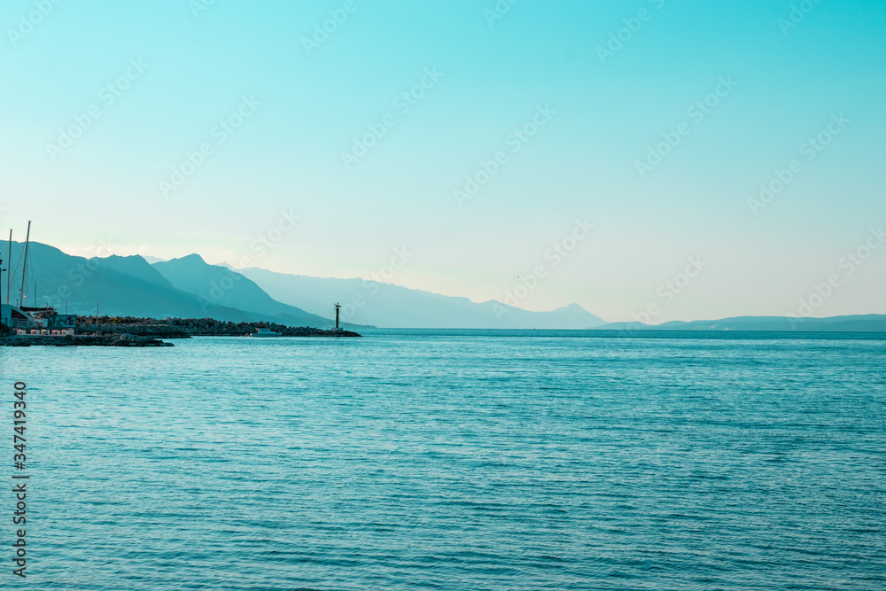 Bright blue morning sunrise on the shore of split, lighthouse in the distance with mountain silhouettes going into the distance