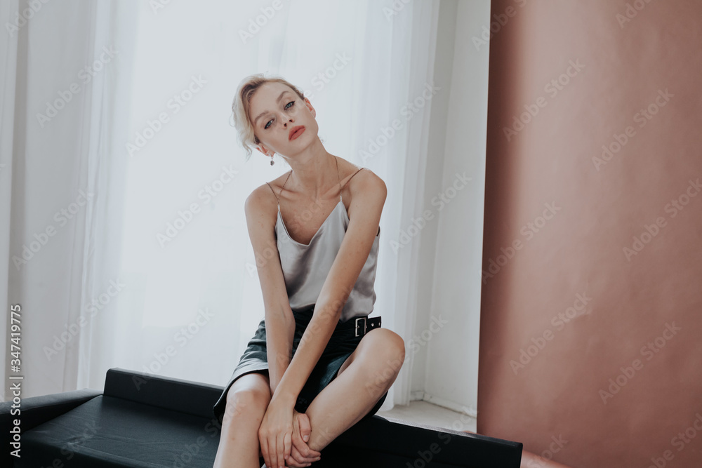 Fototapeta Portret pięknej modnej blondynki na czarnej biurowej kanapie w domu