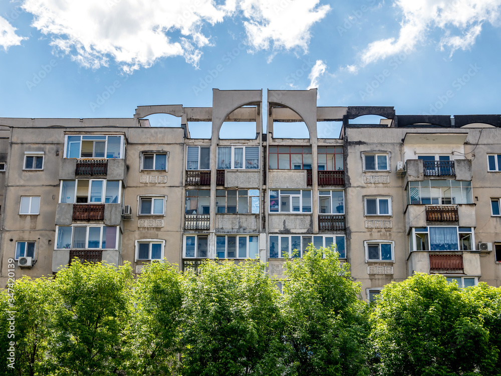 Worn out apartment building from the communist era against blue sky in Bucharest Romania. Ugly traditional communist housing ensemble with green trees wall