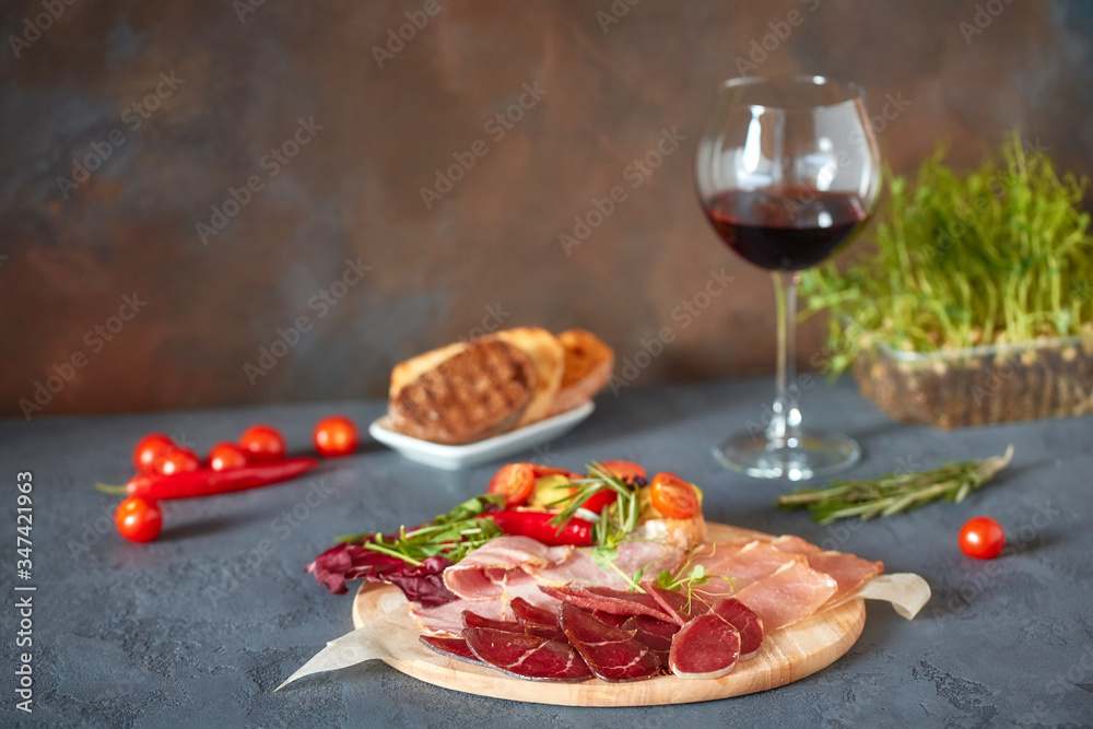 A variety of meat products, laid out on a wooden Board close-up, horizontally, are next to bruschetta with vegetables and fresh herbs A variety of meat products, laid out on a wooden Board close-up, horizontally, are next to bruschetta with vegetables and fresh herbs
