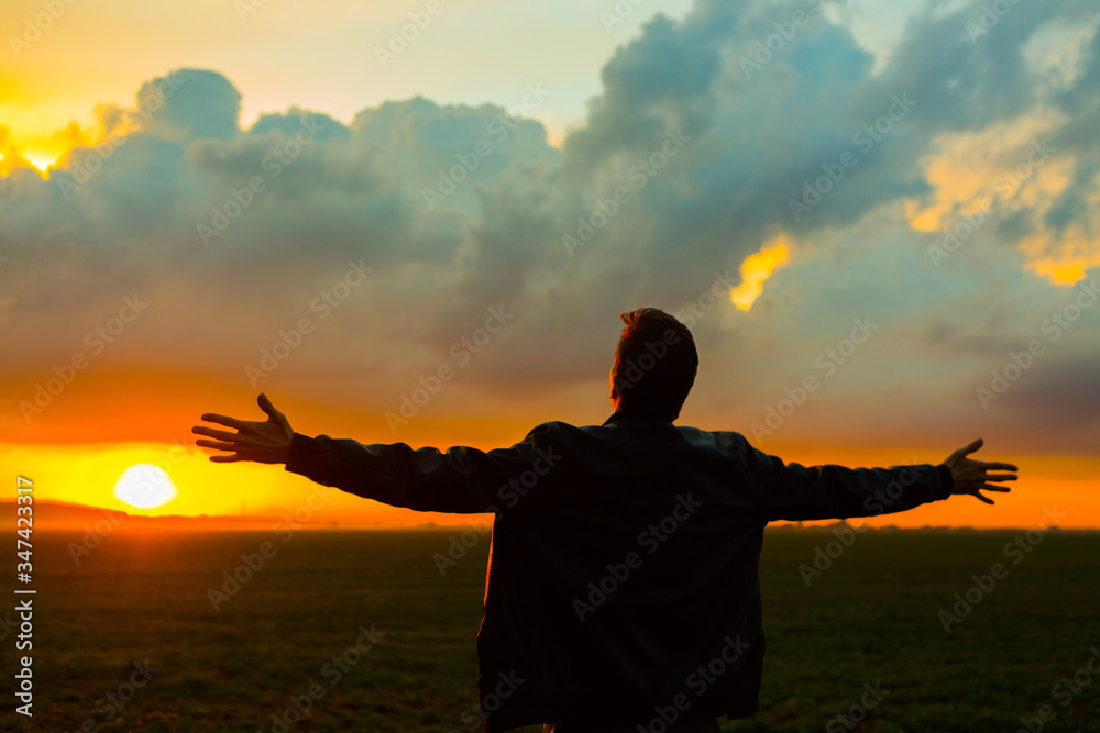 Man in field on beautiful sunset. Silhouette of young man with outstretched arms