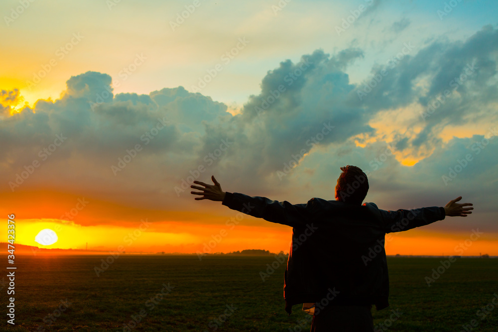 Man in field on beautiful sunset. Silhouette of young man with outstretched arms
