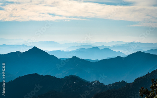 Fototapeta Naklejka Na Ścianę i Meble -  A layer of rolling mountain range with smoke, fog and mist engulfing the rage of hills and mountains in the Hiamalayas of Nepal. a Winter Scenery of hills and valleys with fog in Lamjung of Nepal.