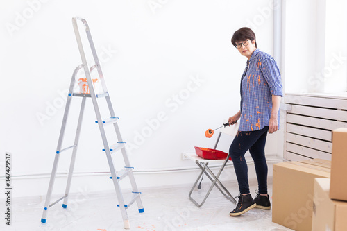 Middle-aged woman painting the walls of new home. Renovation, repair and redecoration concept.