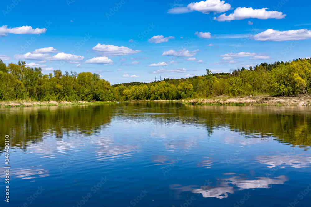 landscape of a beautiful wide river on a sunny day with blue reflection with beautiful clouds in the water