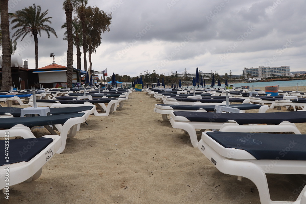 Bad weather. Vaccation near mediterranean Sea in Ayia Napa, Cyprus. Blue and white deck chairs by the sea. Sandy beach in rainy weather. Tourists are in hotel. Ready for damage