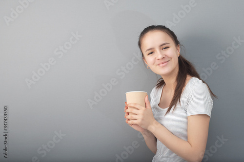 Young woman drinks coffee on gray background