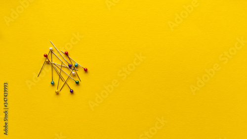 Needles with head on yellow background. Monochrome simple flat lay with pastel texture. Fashion eco concept. Stock photo.