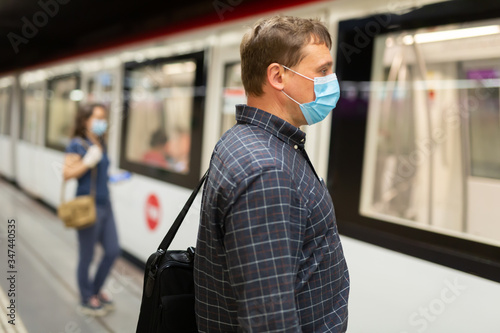 Man in protective medical mask is standing on platform and waiting train in the underground.