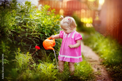 girl watering flowers from a watering can in the garden, happy child, nature, summer in the village