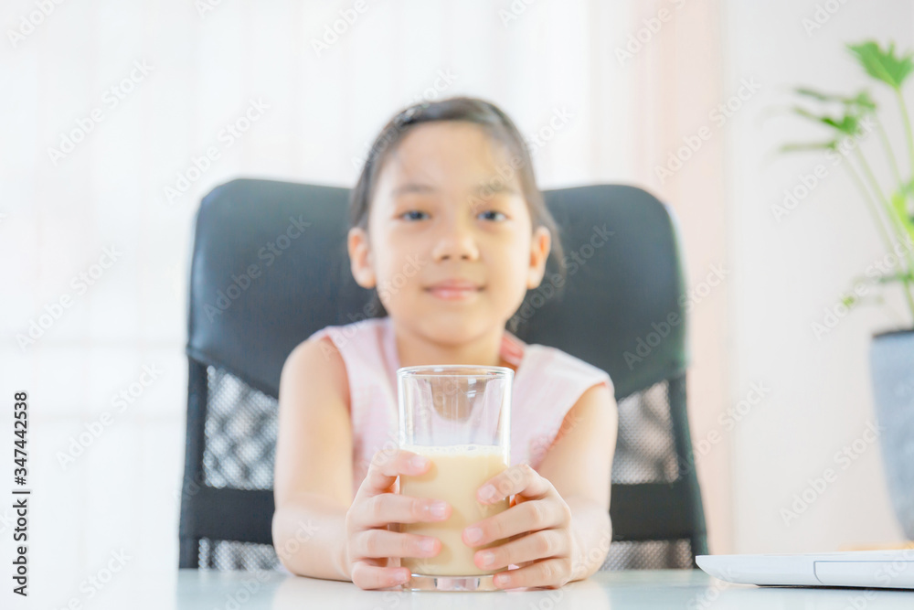 Cheerful little girl smiling and holding glasses of milk, Learn from home concept Cheerful little girl smiling and holding glasses of milk, Learn from home concept