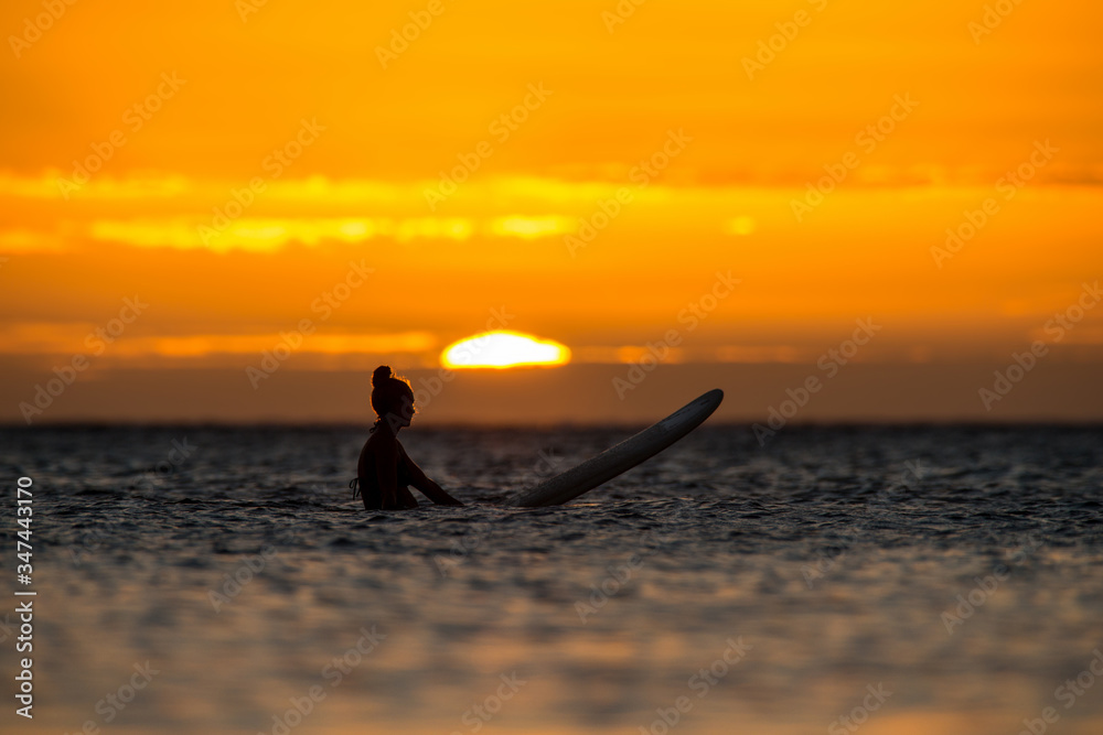 girl surfer waiting for a wave in the open ocean against the backdrop of incredible sunset