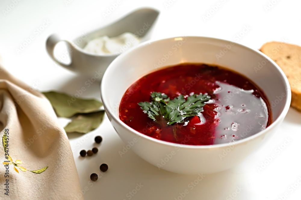 Beetroot soup in white bowl on a white table served with napkin, garlic, pepper, bread and saucy with sour cream. Traditional ukrainian, russian soup borscht with greens. Beetroot soup in white bowl on a white table served with napkin, garlic, pepper, bread and saucy with sour cream. Traditional ukrainian, russian soup borscht with greens.
