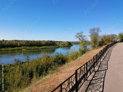 Paved embankment of a quiet wide river with a forest