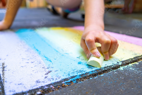 Girl drawing rainbow with chalk on pavement