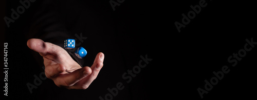 Male hand throwing blue dice cubes in the air against black background - narrow banner with copy space