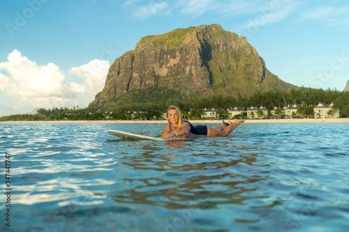 A beautiful girl rowing on a surfboard in the ocean against the backdrop of a picturesque mountain